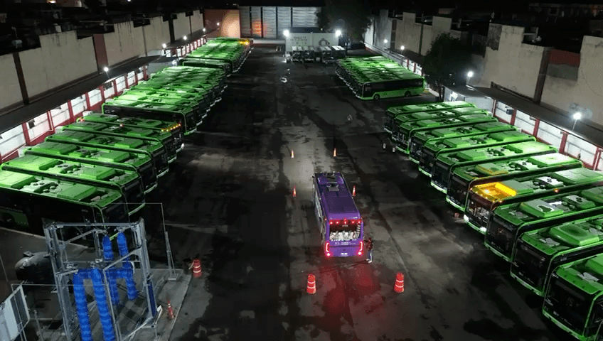 Vista nocturna de un patio de autobuses, con filas de unidades y personal junto a un vehículo en el pasillo central.